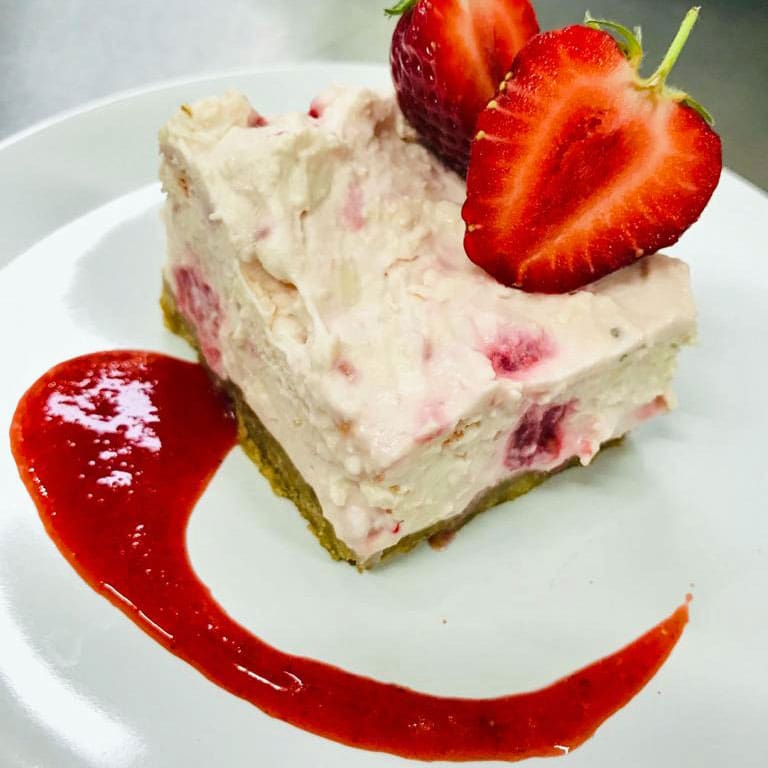 White-chocolate-and-raspberry-cheesecake-with-strawberry-coulis-sq-web piece of cheesecake on plate